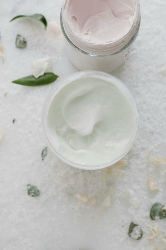 pexels-photo-6690249-6690249 Top view of elegant skincare creams in glass jars with natural elements on a soft white background.