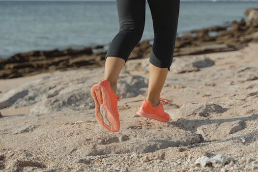 pexels-photo-5928324-5928324 Adult jogging on the beach with vibrant orange shoes, showcasing active lifestyle.